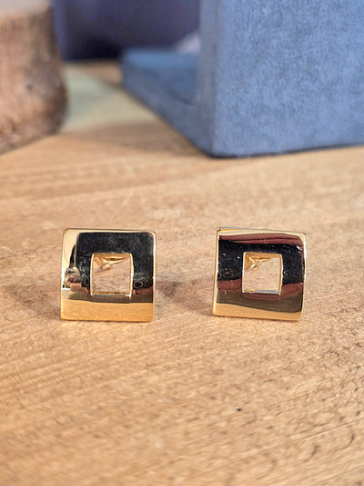 Gold square earrings on a textured surface with a blue box in the background