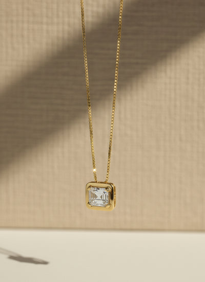 Gold necklace with a rectangular diamond pendant on a light gray background